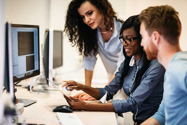 Three people look at a laptop