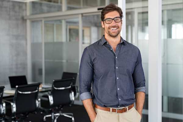 A man wearing a button down shirt and khaki pants stands in an office.