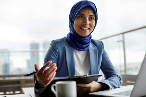 A female job applicant sits at a desk in front of a laptop.