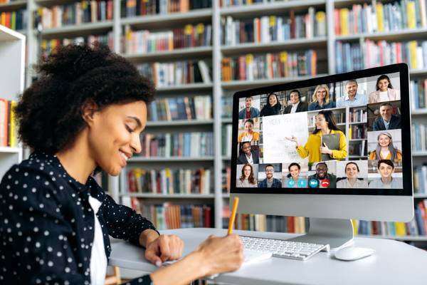 A female student sits in front of a computer screen showing an online class with a diverse group of students.