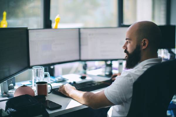 An IT professional sits at a desk with multiple computer monitors