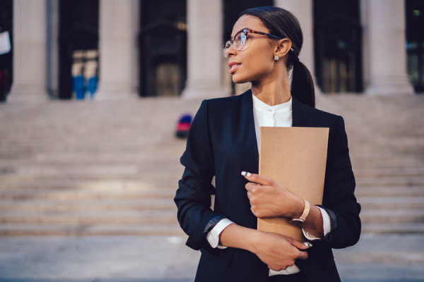 Pensive female paralegal holding a folder on the steps of a courthouse.