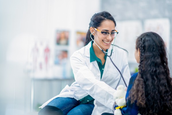 A nurse practitioner uses her stethoscope to listen to her young patient's chest.