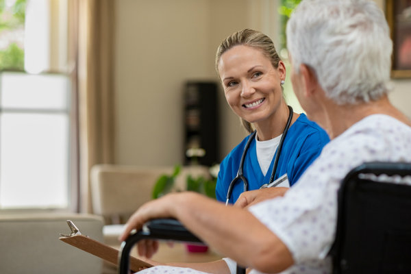 A woman nurse with a clipboard sitting down with an elderly patient in a wheelchair.