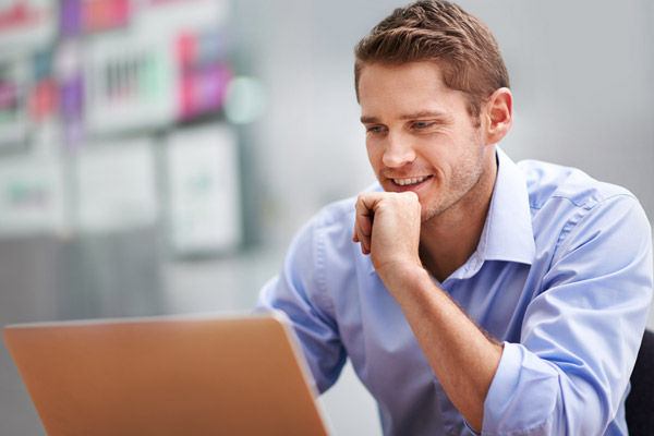 A man sits at a desk while looking at a laptop