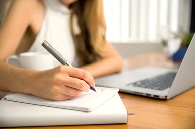 A woman writes her to-do list in a notebook.