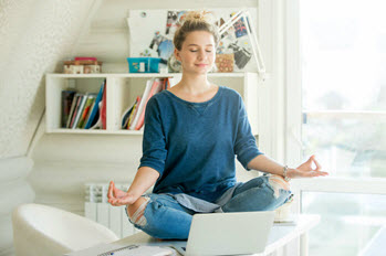 A woman sits cross-legged on a desk while meditating.