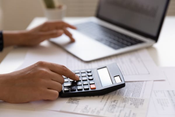 Close up of woman using a calculator and entering information on a laptop.