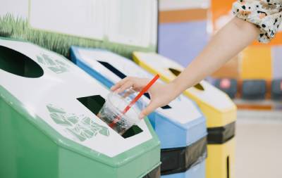 A person puts a cup in a recycling bin
