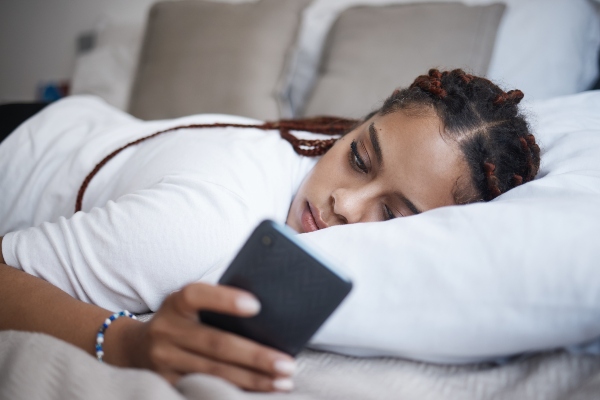 A woman looks at her phone while lying in bed.