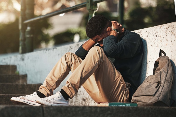 A young man with his head lowered sits on some stairs.